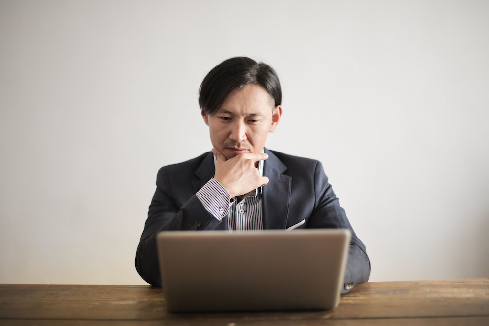 パソコンの前で悩んでいる男性の画像。