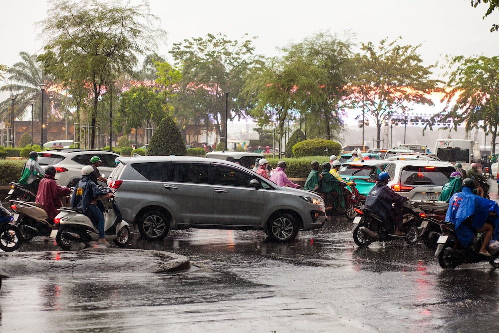激しい雨の中、バイクと車が行き交う賑やかな通り、都市の風景の画像。