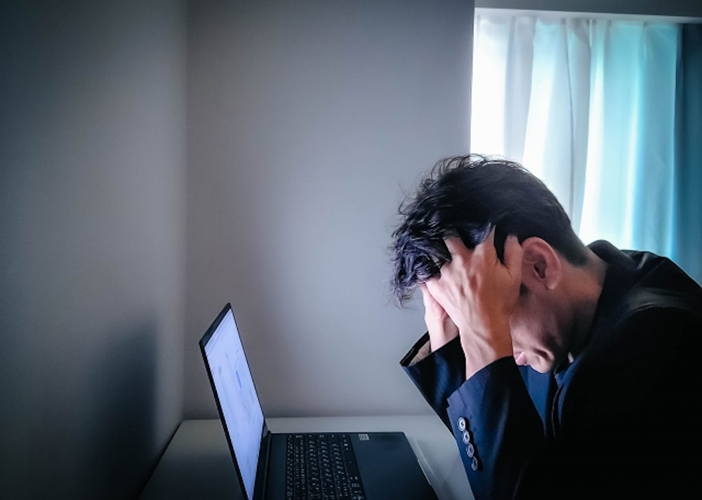 パソコンの前で頭を抱え落胆している男性の画像。
